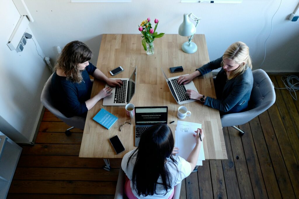 Photo by CoWomen three women sitting around table using laptops